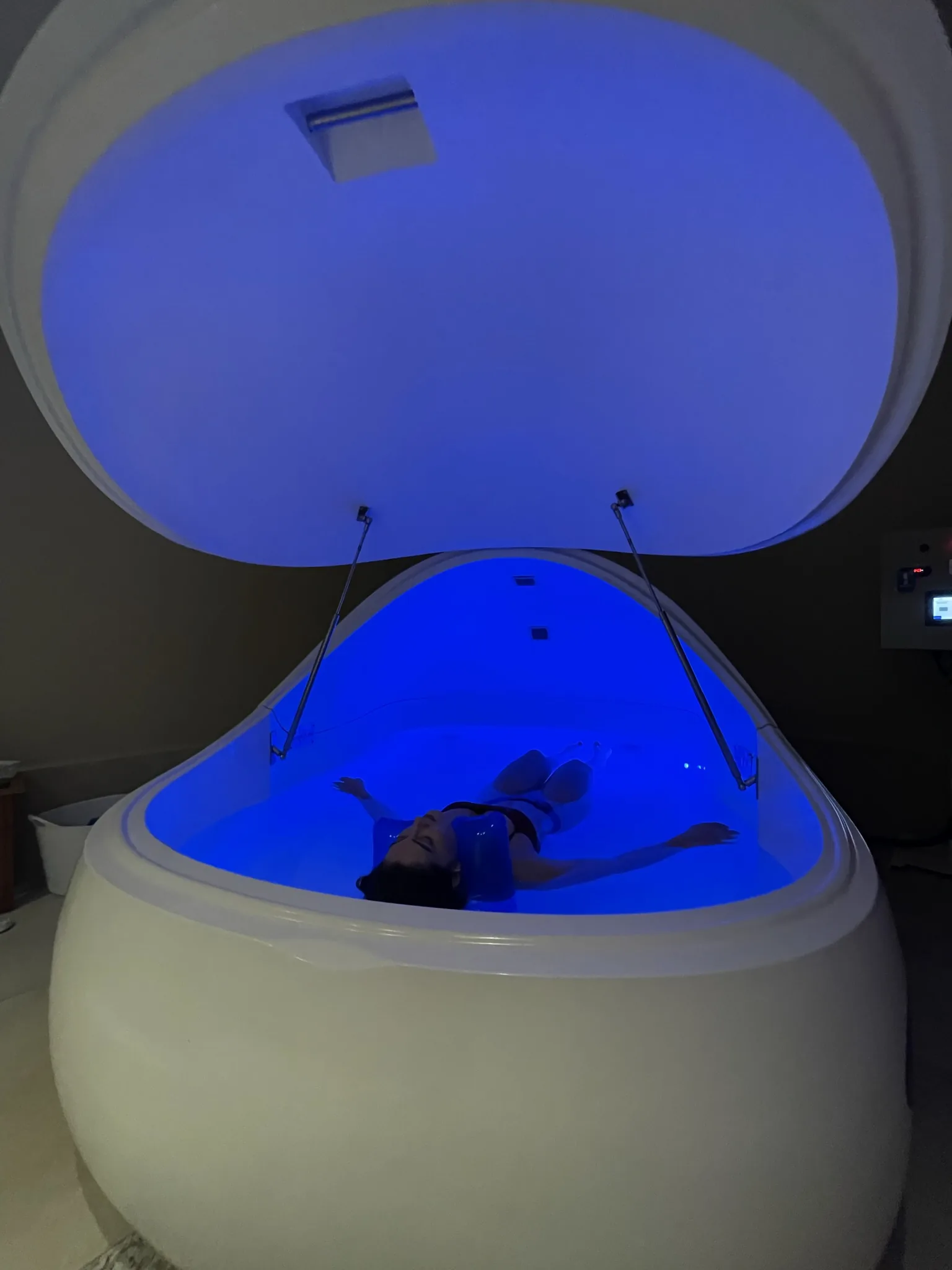 Cápsula de flutuação aberta, iluminada em azul, com cliente flutuando